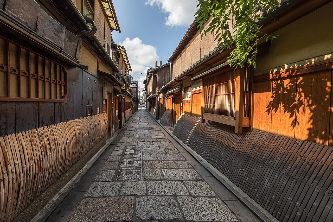 A narrow stone-paved street in Gion, Kyoto, lined with wooden townhouses hung with sudare reed blinds